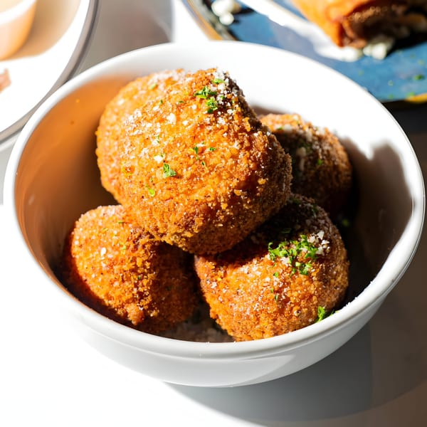 A white bowl filled with golden-brown, breaded arancini, topped with grated cheese and parsley.