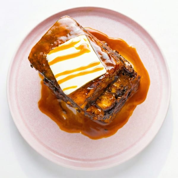 Sticky toffee pudding with a pat of butter and caramel drizzle on a pink plate.