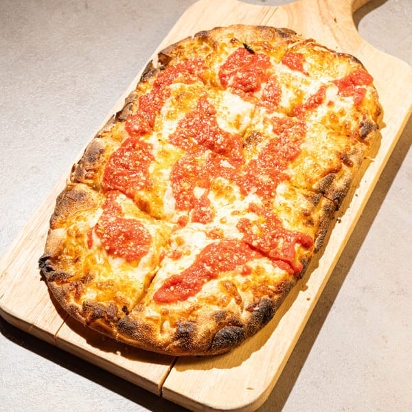 Rectangular pizza with red sauce and melted cheese on a wooden serving board.