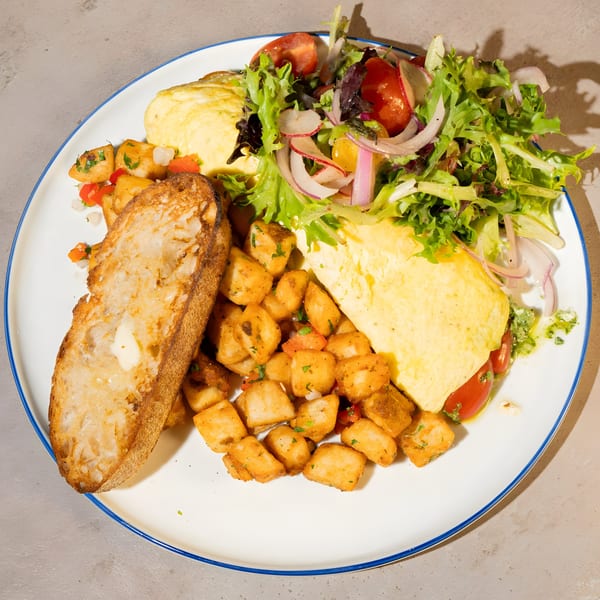 A breakfast plate with a fluffy omelet, crispy home fries, fresh salad, and buttered toast.