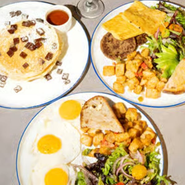 Three plates of breakfast food, including pancakes, eggs, sausage, potatoes, and salad.