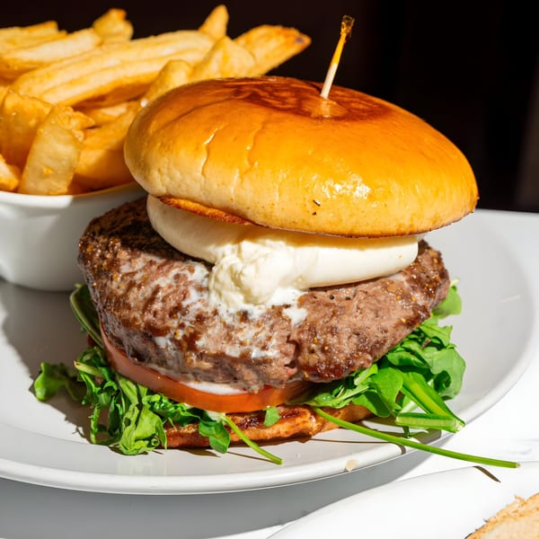 A Bite Food & Coffee Co burger with melted cheese, tomato, and arugula, served with fries.