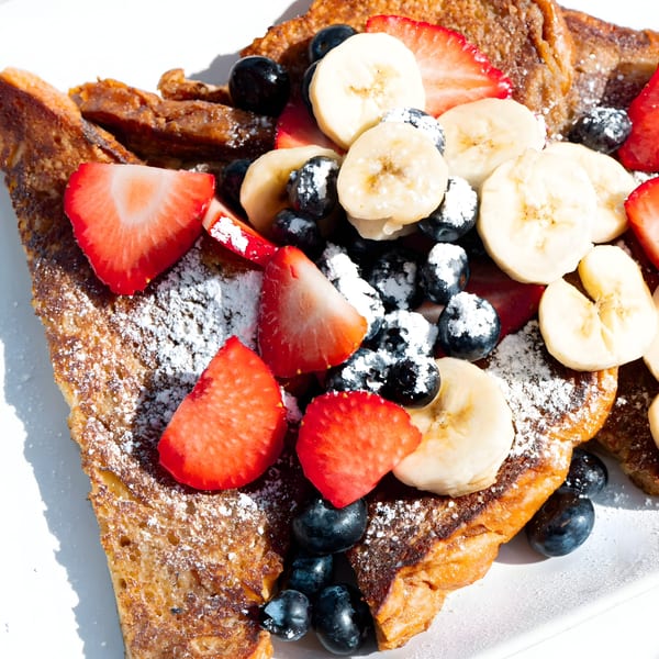 Golden French toast topped with sliced strawberries, bananas, blueberries, and powdered sugar.