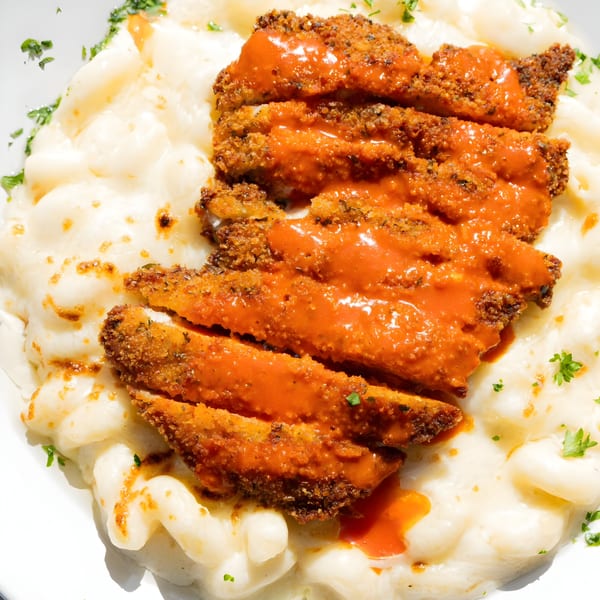 Crispy fried chicken strips with orange sauce over creamy macaroni and cheese, garnished with parsley.