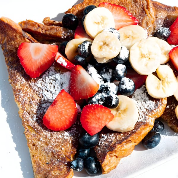 Golden French toast topped with fresh strawberries, blueberries, banana slices, and powdered sugar.